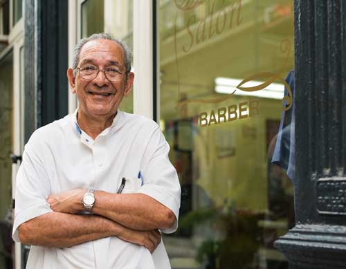 Older Hispanic Man standing in front of his barber shop